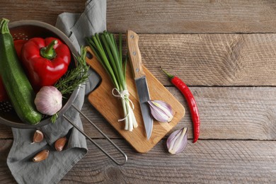 Photo of Cooking ratatouille. Vegetables, rosemary and knife on wooden table, flat lay