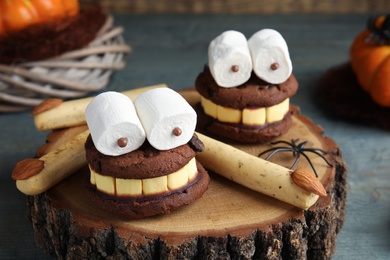 Photo of Delicious desserts decorated as monsters on stump, closeup. Halloween treat