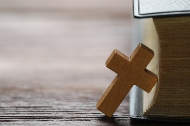 Photo of Wooden Christian cross and Bible on table, closeup. Space for text