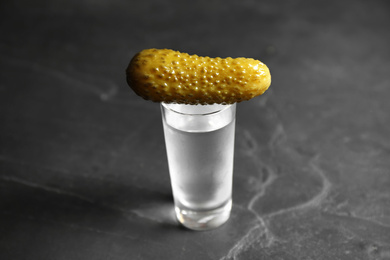 Photo of Cold Russian vodka with pickle on black table, closeup