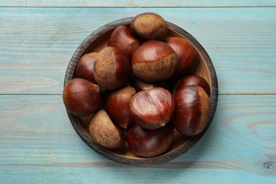 Photo of Roasted edible sweet chestnuts on light blue wooden table, top view