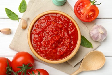 Photo of Homemade tomato sauce in bowl, spoon and fresh ingredients on white wooden table, flat lay