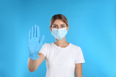 Photo of Woman in protective mask showing stop gesture on light blue background. Prevent spreading of COVID‑19