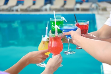 Friends clinking glasses with fresh summer cocktails near swimming pool, closeup