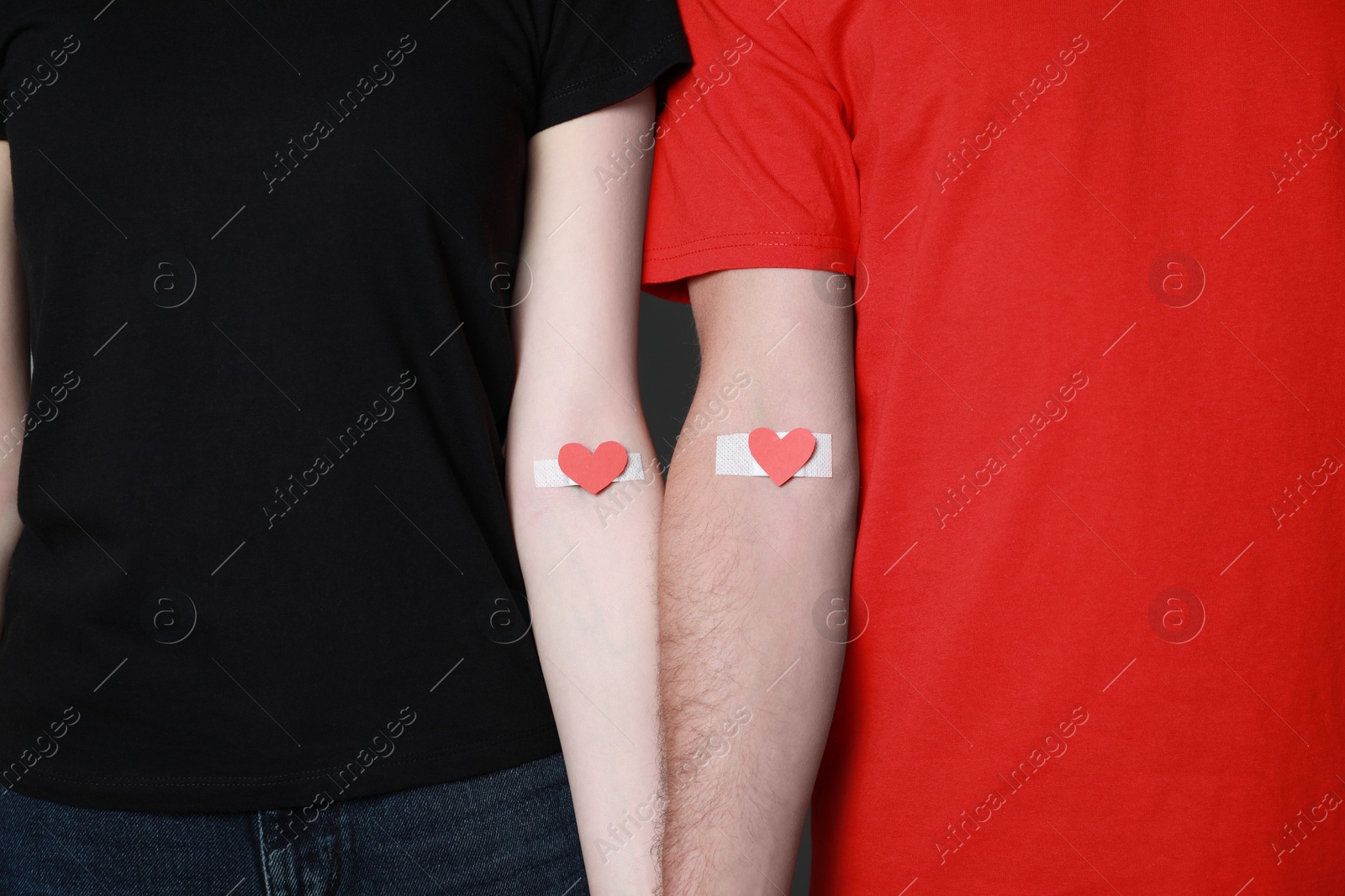 Photo of Blood donation concept. Couple with adhesive plasters on arms against grey background, closeup