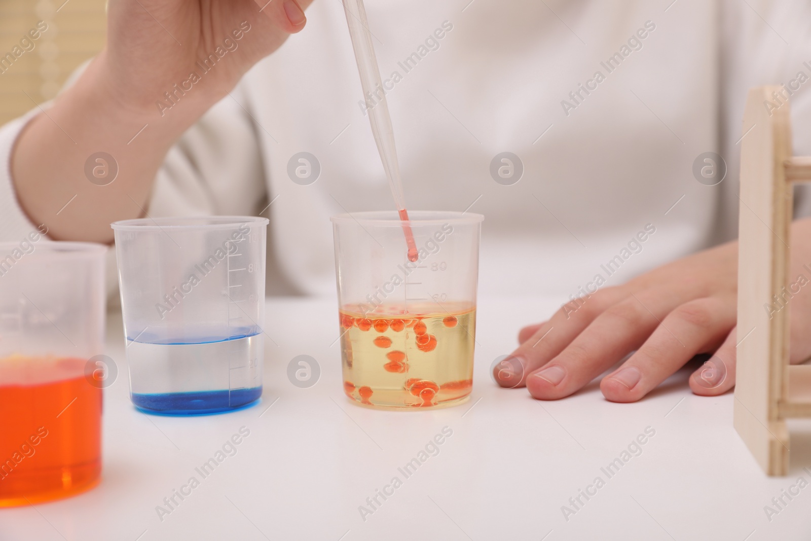 Photo of Girl mixing colorful liquids at white table indoors, closeup. Chemical experiment set for kids