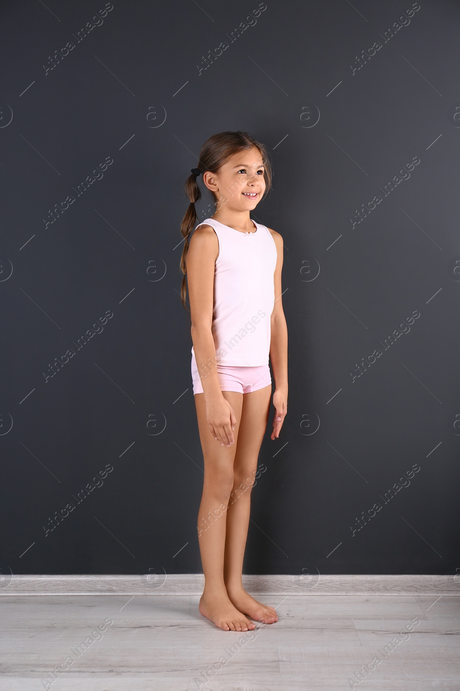 Photo of Cute little girl in underwear near dark wall