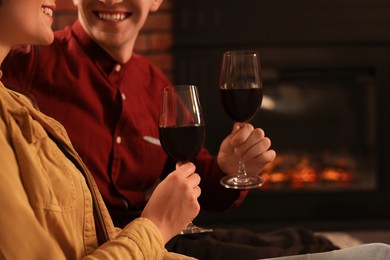 Happy lovely couple with glasses of wine resting together near fireplace at home, closeup