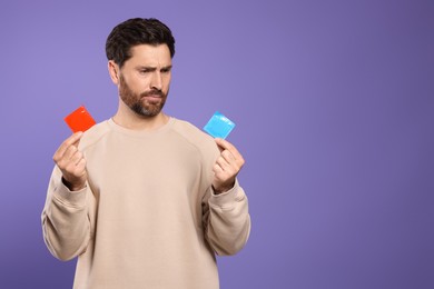 Photo of Confused man holding condoms on purple background, space for text. Safe sex