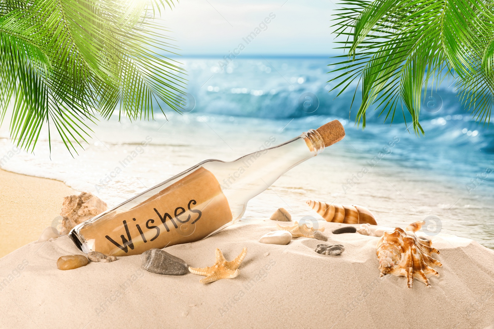 Image of Corked glass bottle with rolled paper note and seashells on sandy beach with palms near ocean