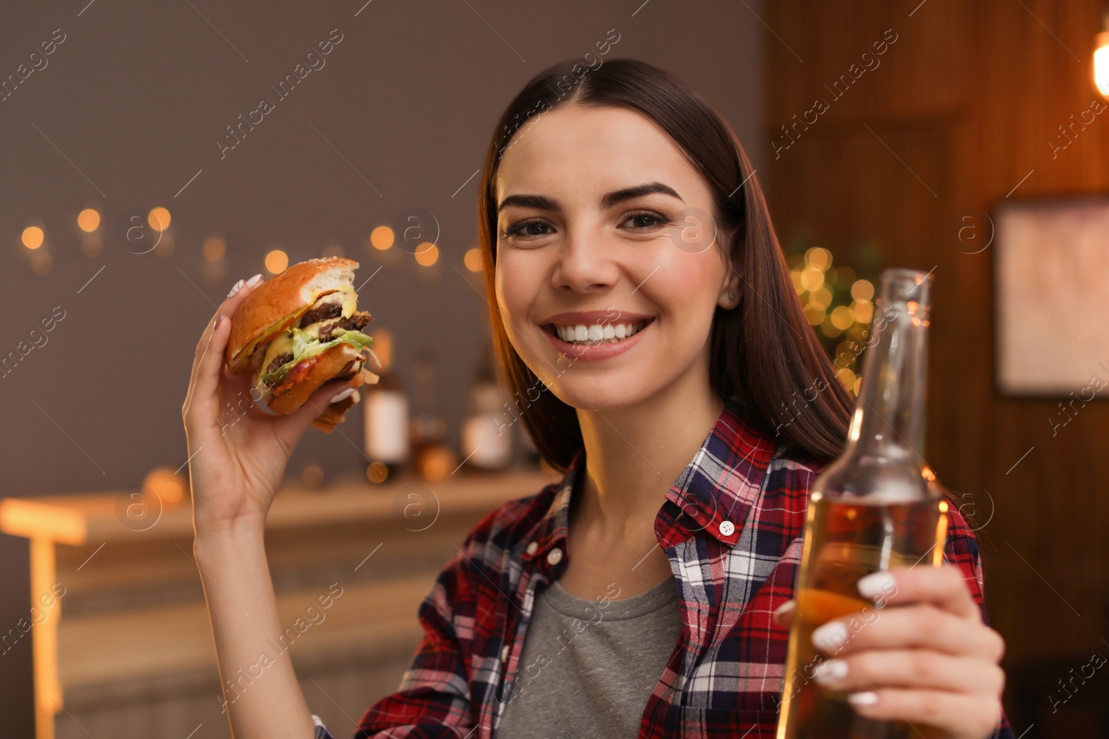 Photo of Young woman with beer eating tasty burger in cafe