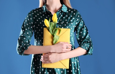 Woman holding elegant clutch with spring flowers on blue background, closeup