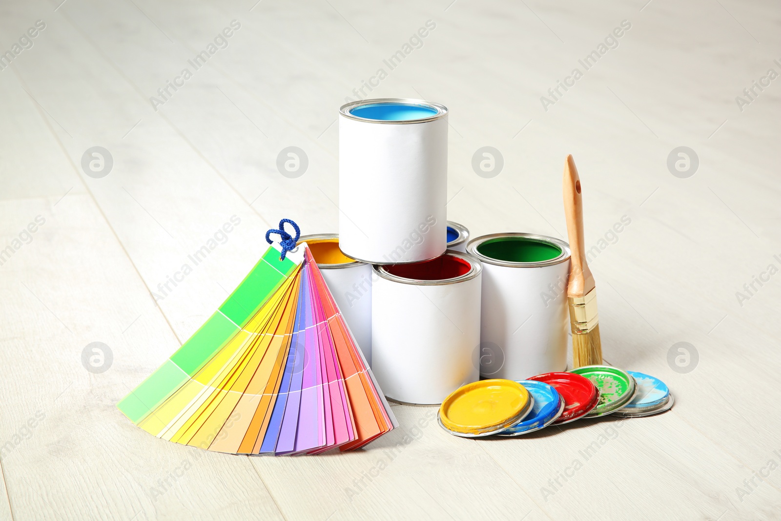 Photo of Cans of paint, brush and color palette on wooden floor indoors