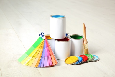 Photo of Cans of paint, brush and color palette on wooden floor indoors