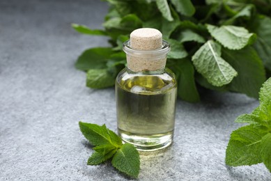 Photo of Bottle of essential oil and mint on grey table, closeup