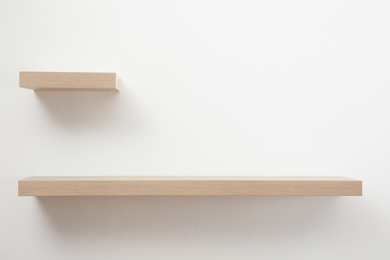 Empty stylish wooden shelves on light wall