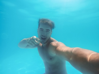 Photo of Handsome young man swimming in pool, underwater view