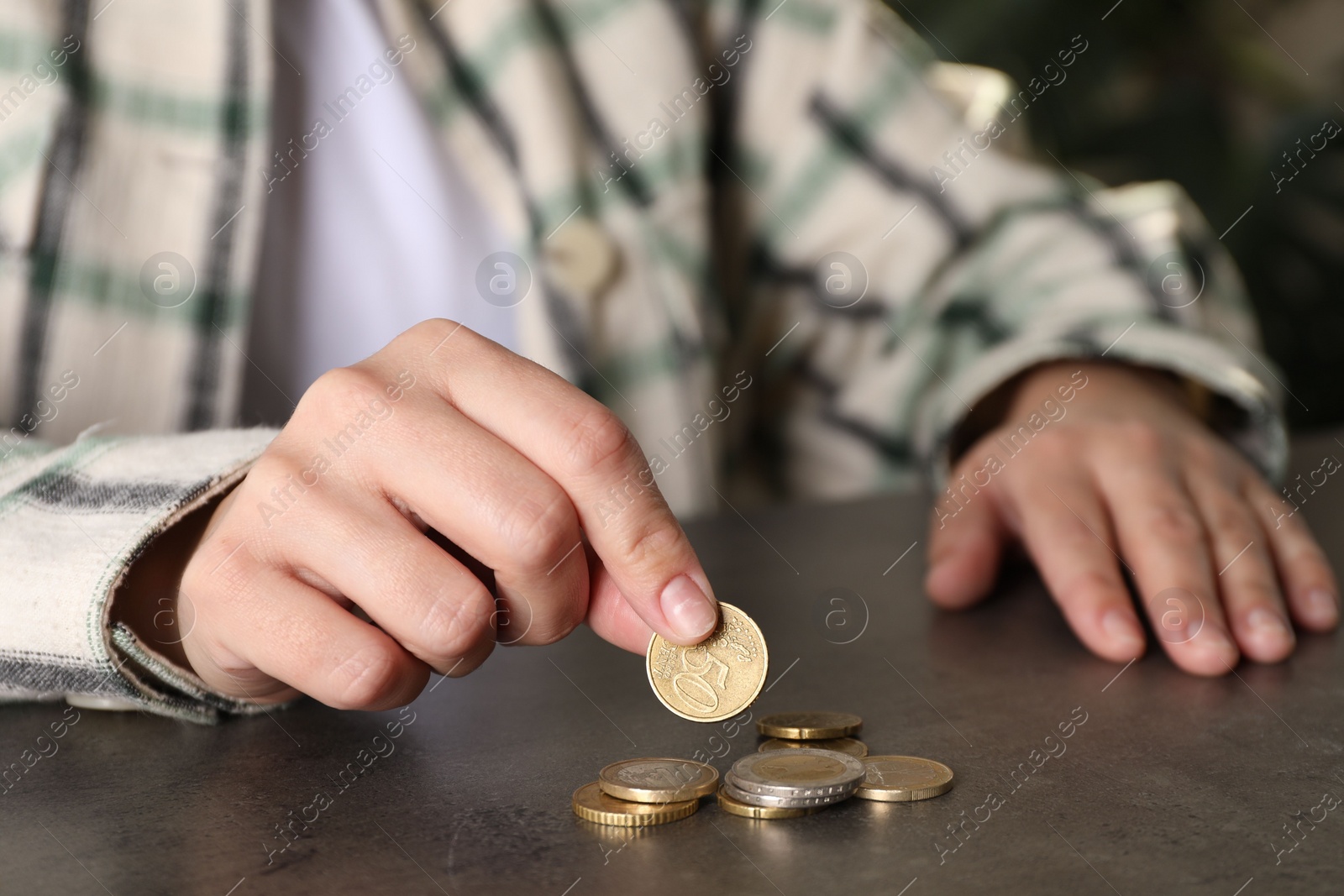 Photo of Poor woman counting coins at grey table indoors, closeup