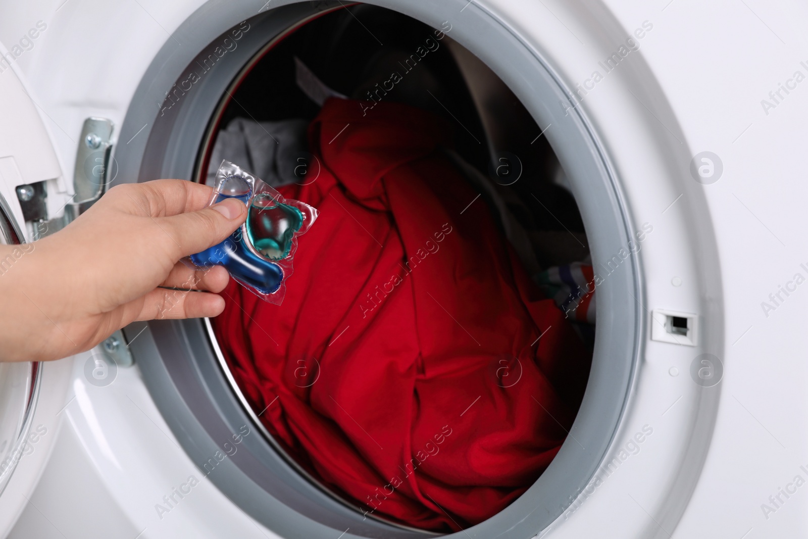 Photo of Woman putting laundry detergent capsule into washing machine, closeup