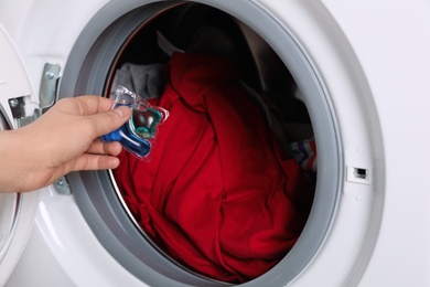 Woman putting laundry detergent capsule into washing machine, closeup