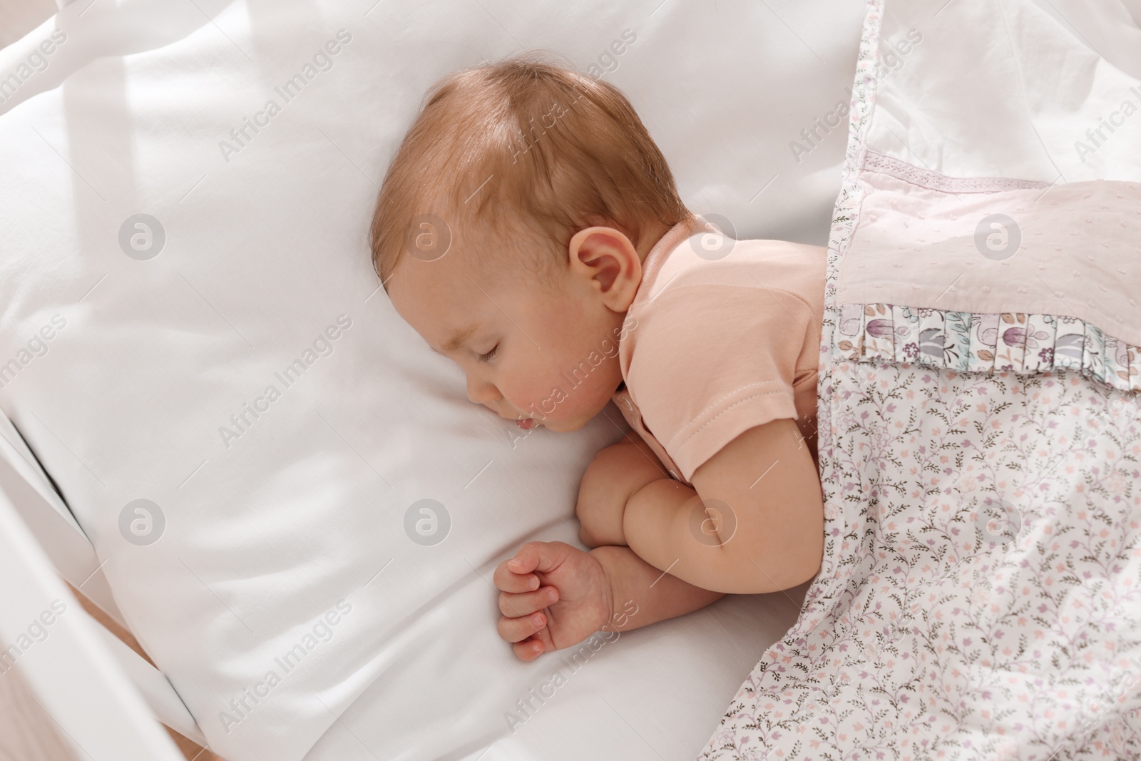 Photo of Cute little baby sleeping in soft crib, top view