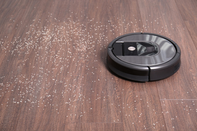 Photo of Removing groats from wooden floor with robotic vacuum cleaner at home. Space for text