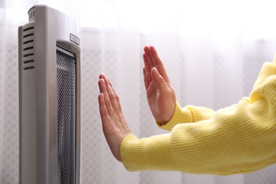 Woman warming hands near heater indoors, closeup