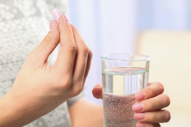 Woman holding pill and glass of water on blurred background, closeup. Space for text