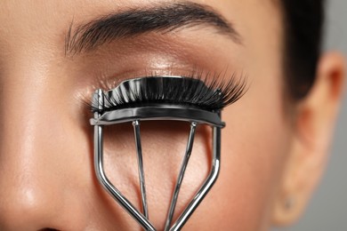 Photo of Young woman using eyelash curler on grey background, closeup