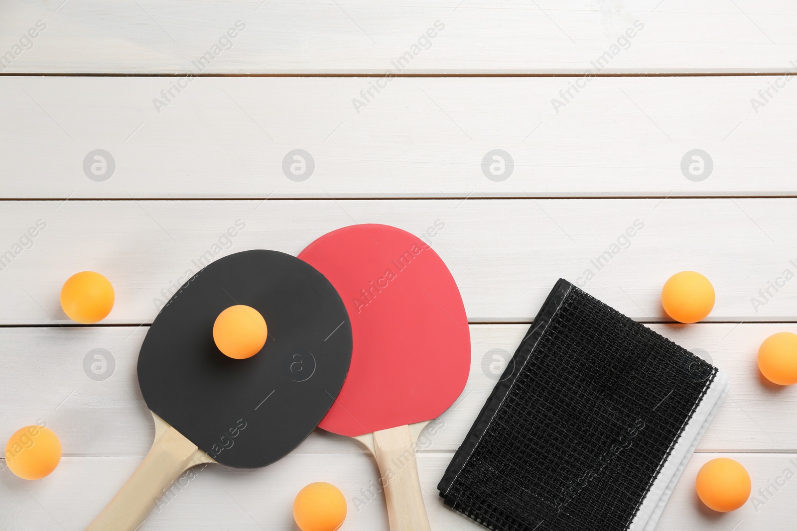 Photo of Ping pong rackets, net and balls on white wooden table, flat lay. Space for text