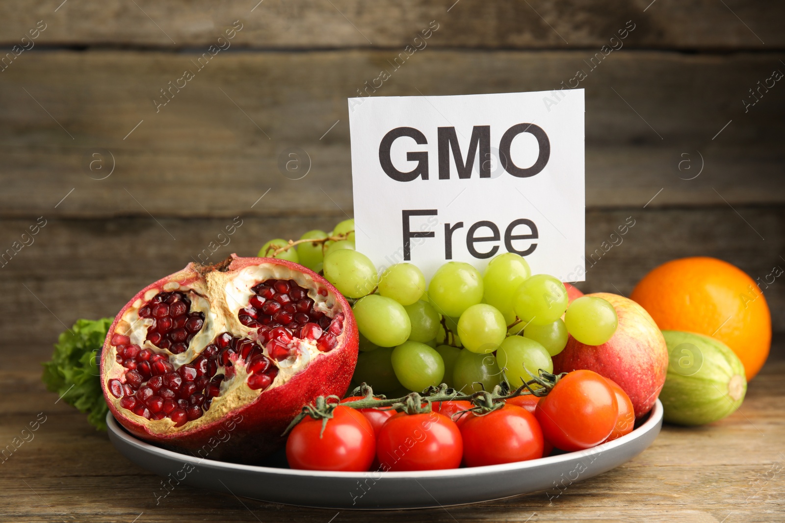 Photo of Fresh fruits, vegetables and card with text GMO Free on wooden table