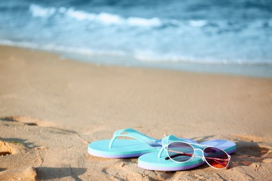 Photo of Stylish flip flops and sunglasses on sand near sea, space for text. Beach accessories