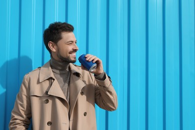 Handsome man holding tin can with beverage near light blue wall. Space for text