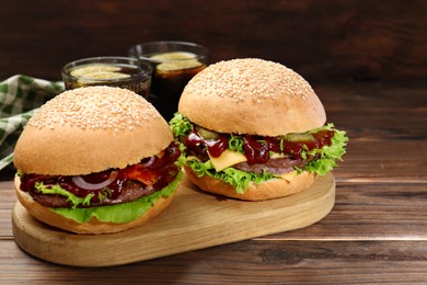 Board with delicious cheeseburgers on wooden table, closeup