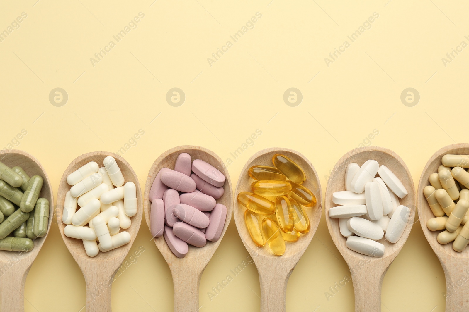 Photo of Different vitamin pills in spoons on pale yellow background, flat lay. Space for text