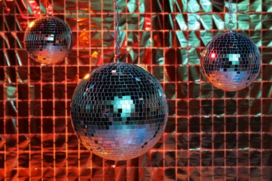 Photo of Shiny disco balls against foil party curtain under color lights