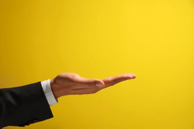 Man holding something in hand on yellow background, closeup. Space for text