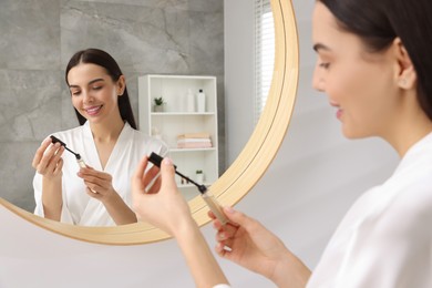 Photo of Beautiful young woman with gel for eyelashes near mirror in bathroom