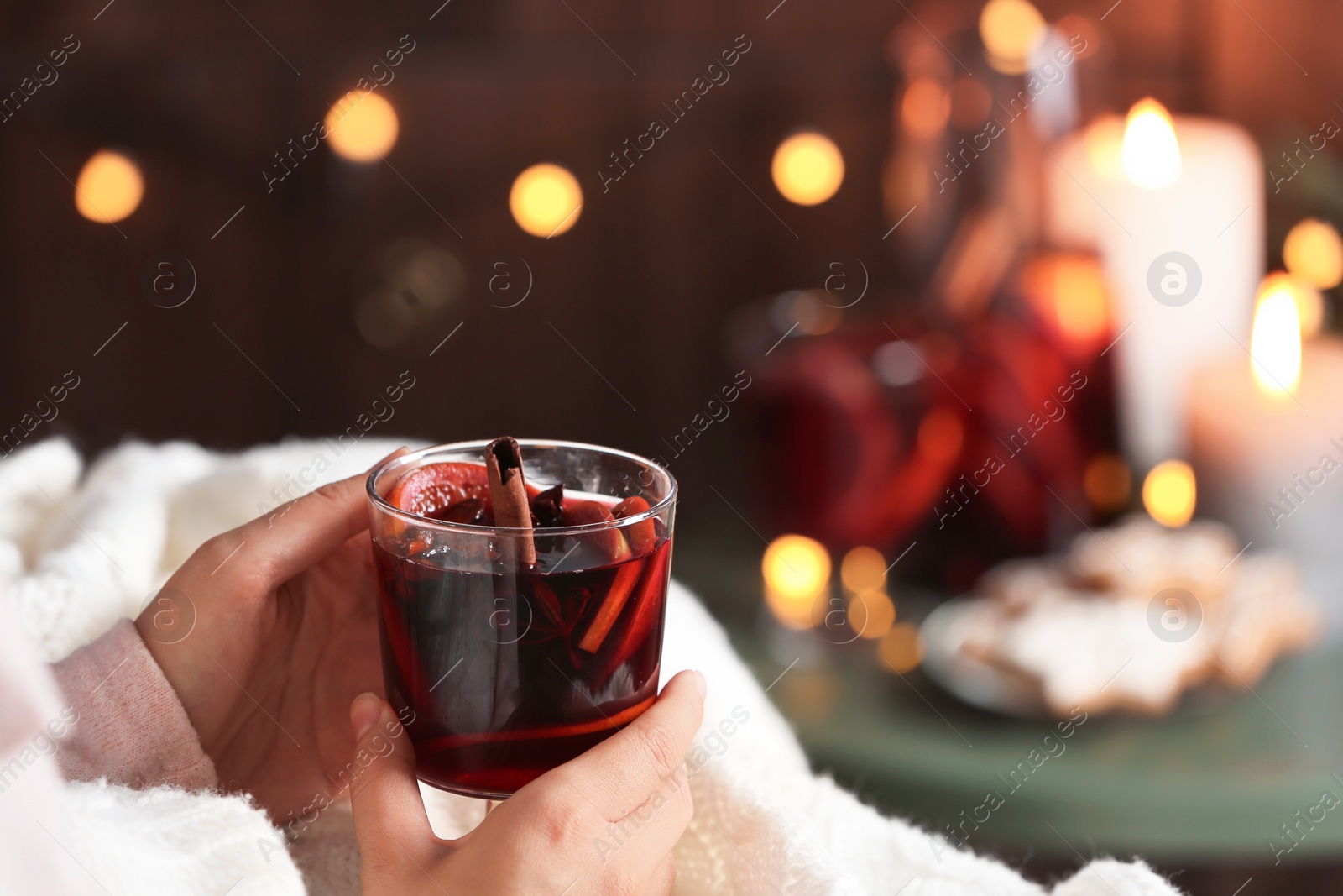 Photo of Woman with glass of mulled wine at home, focus on hands. Space for text