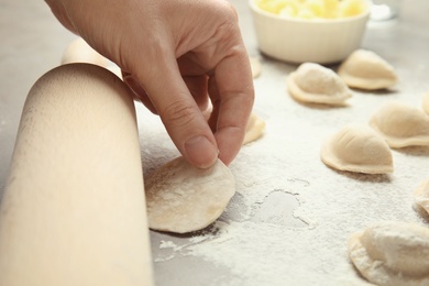 Photo of Woman with rolling pin cooking delicious dumplings at table, closeup
