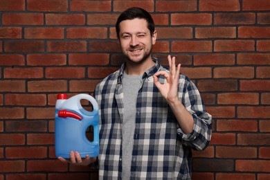 Photo of Man holding canister with blue liquid and showing OK gesture near brick wall