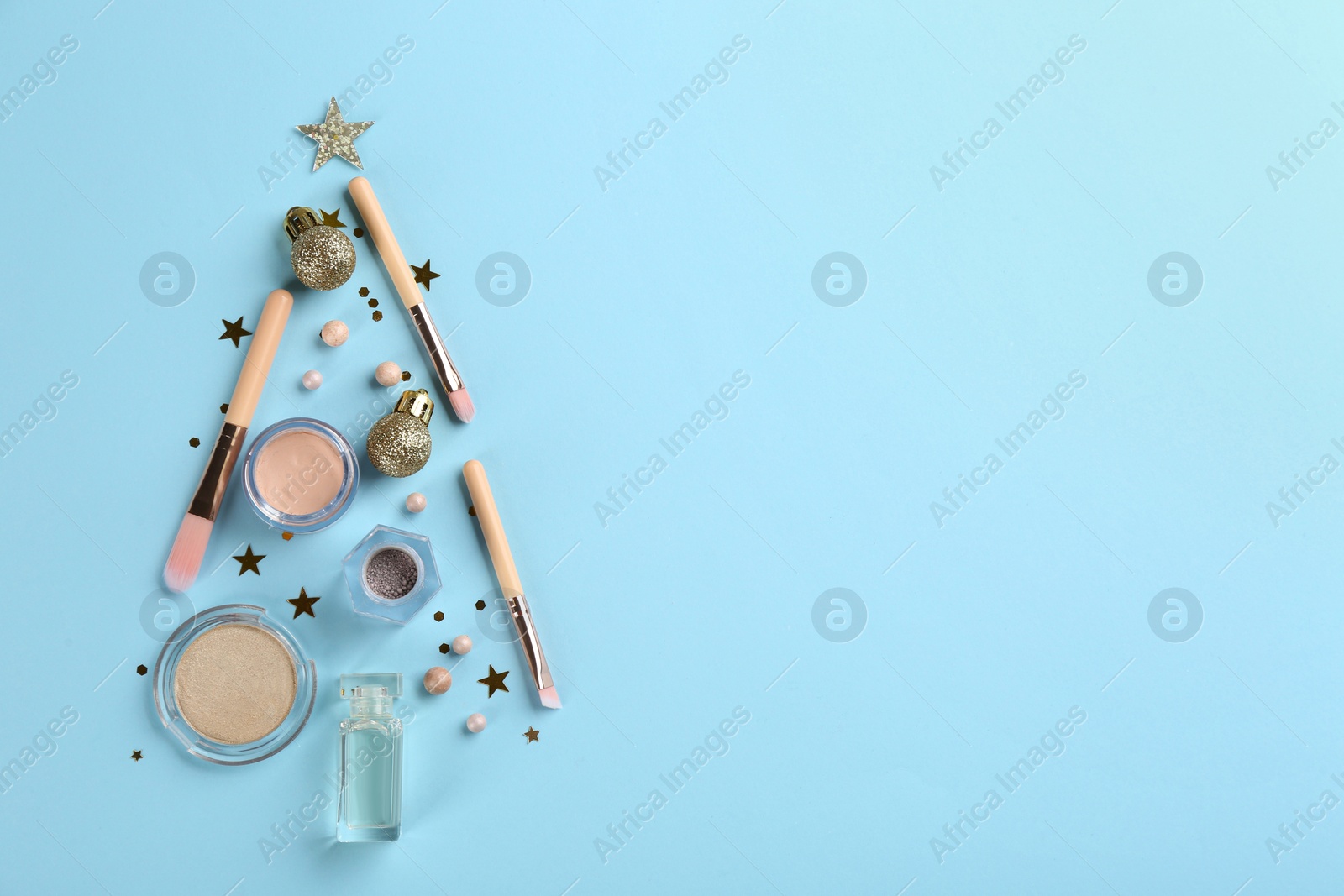 Photo of Christmas tree shape of decorative cosmetic products on light blue background, flat lay with space for text. Winter care