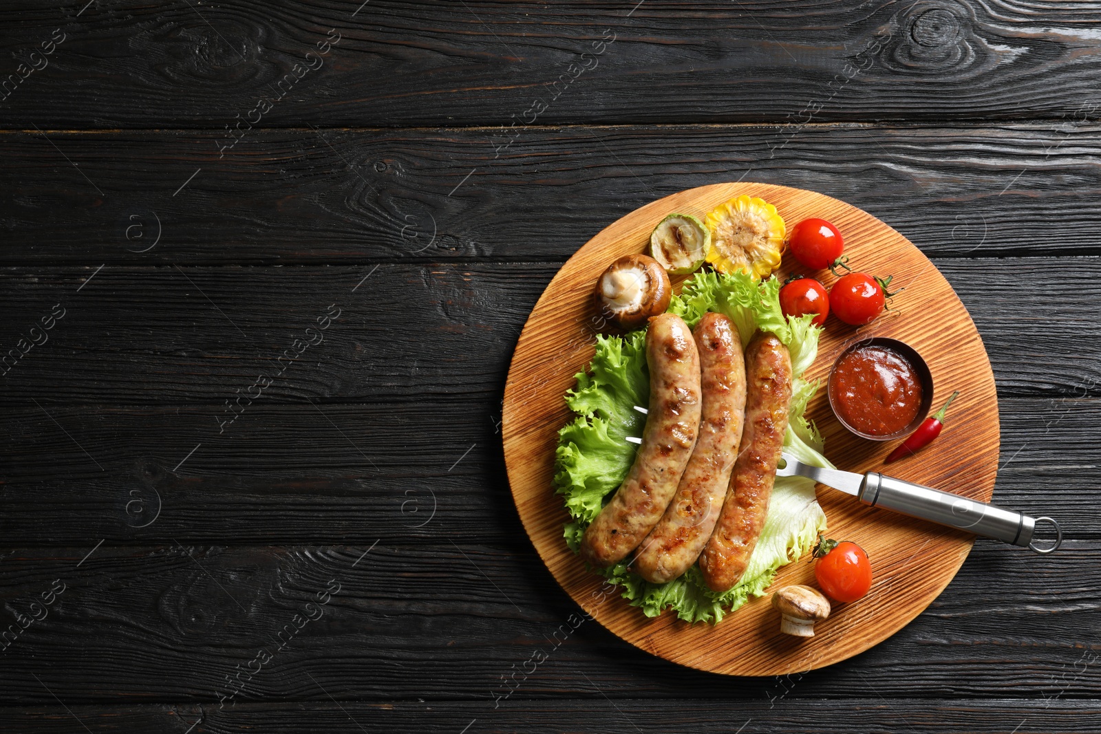 Photo of Delicious barbecued sausages served with vegetables and sauce on dark background. Space for text