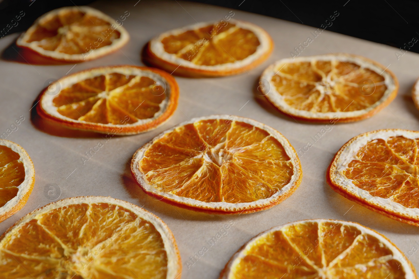 Photo of Many dry orange slices on parchment paper, closeup