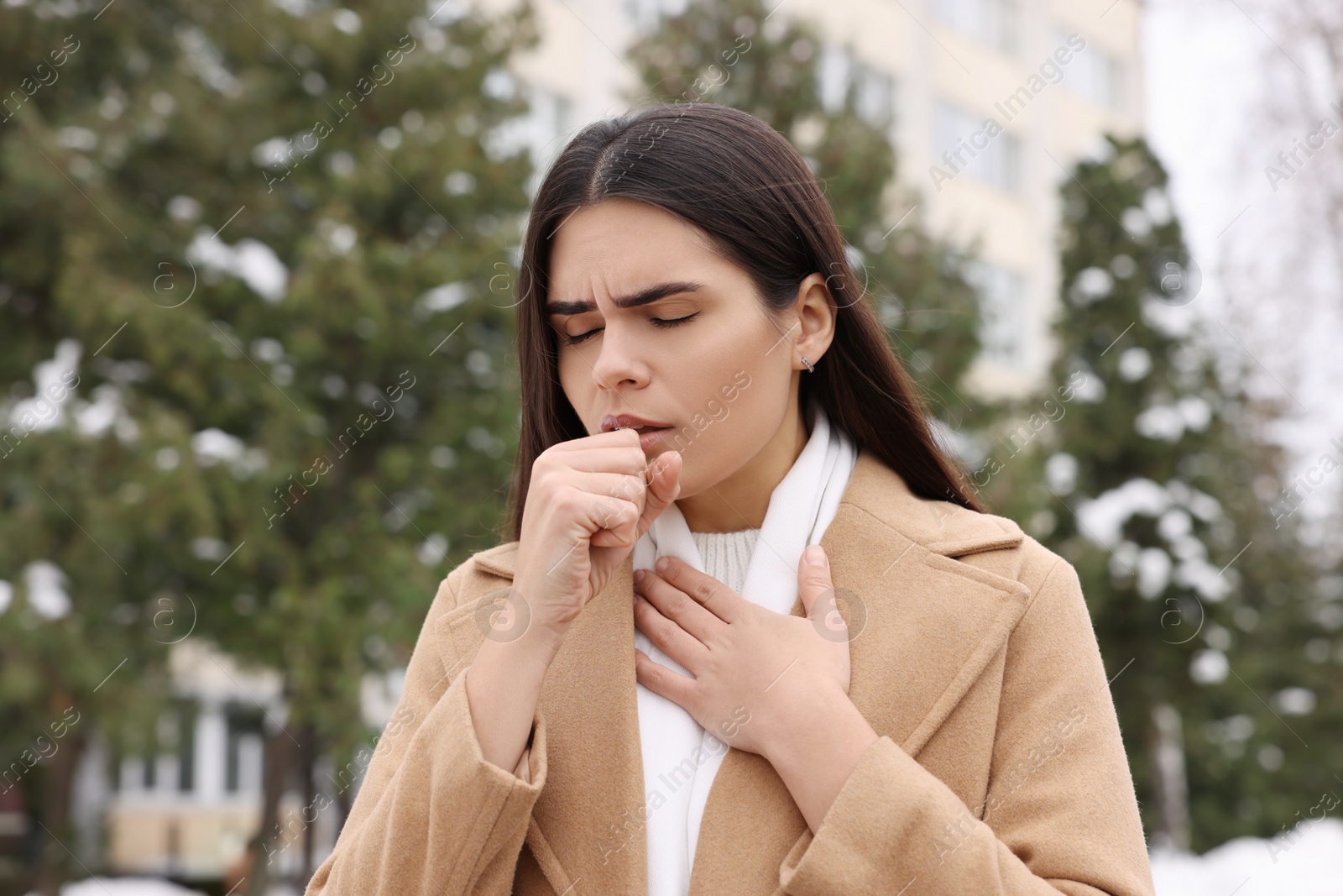 Photo of Woman in coat coughing outdoors. Cold symptoms