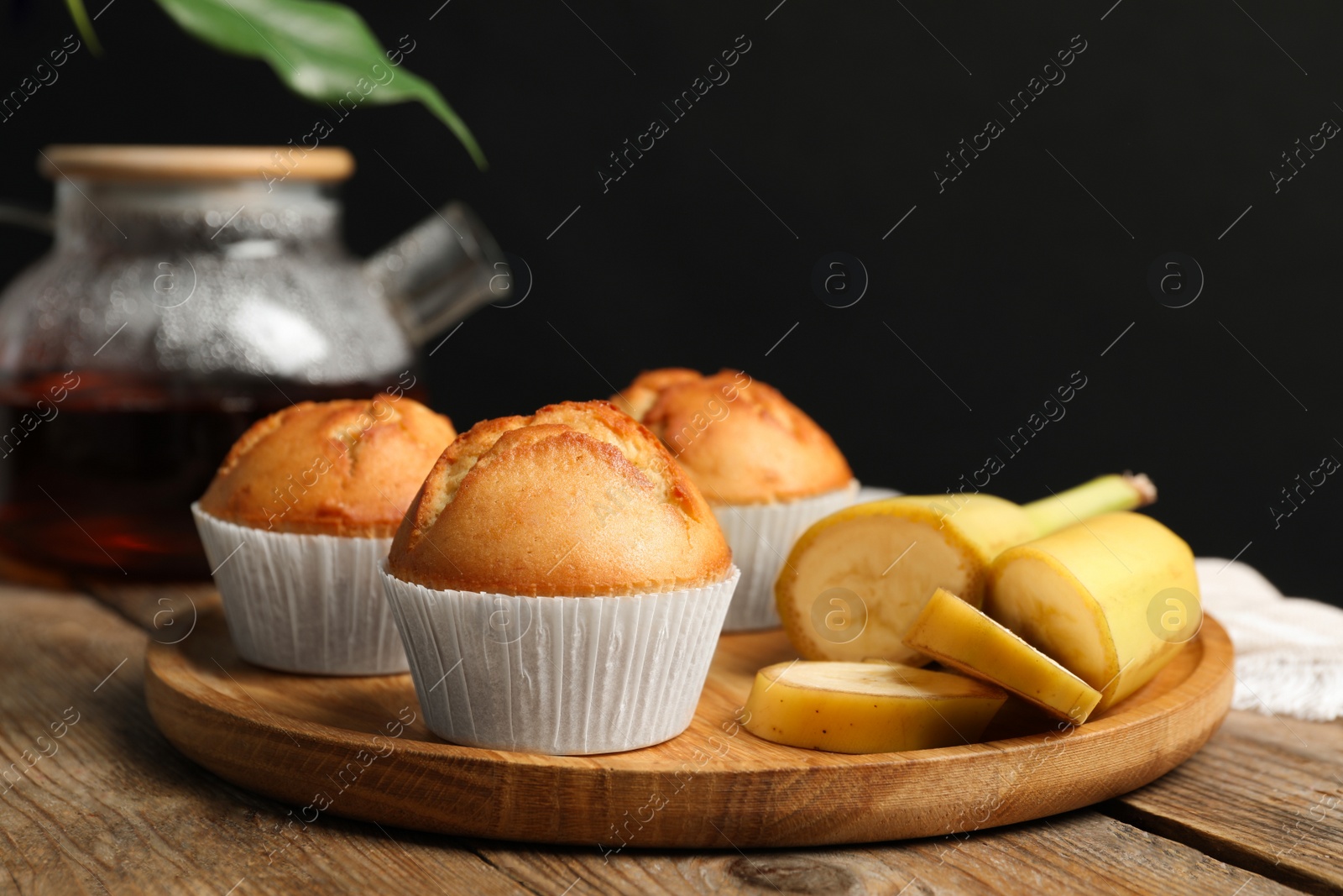 Photo of Tasty muffins served with banana slices on wooden table against dark background