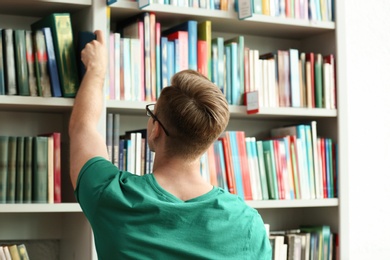 Young man taking book from shelving unit in library