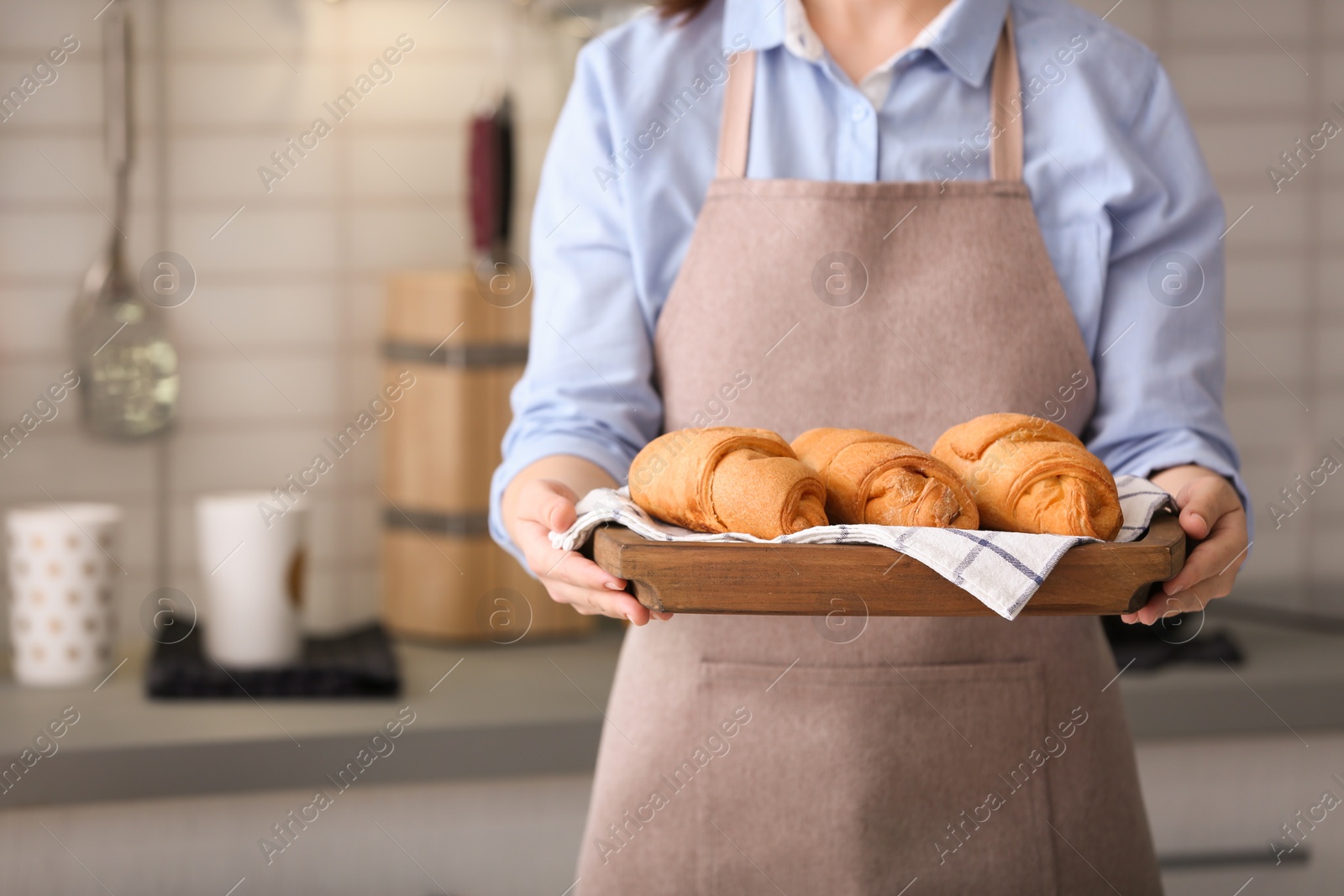 Photo of Woman holding wooden tray with delicious croissants in kitchen, closeup