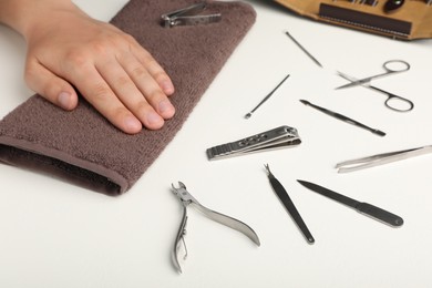 Man holding hand on towel near set of manicure tools at white table, closeup