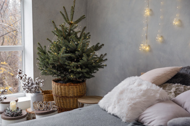 Photo of Little Christmas tree with fairy lights in bedroom interior